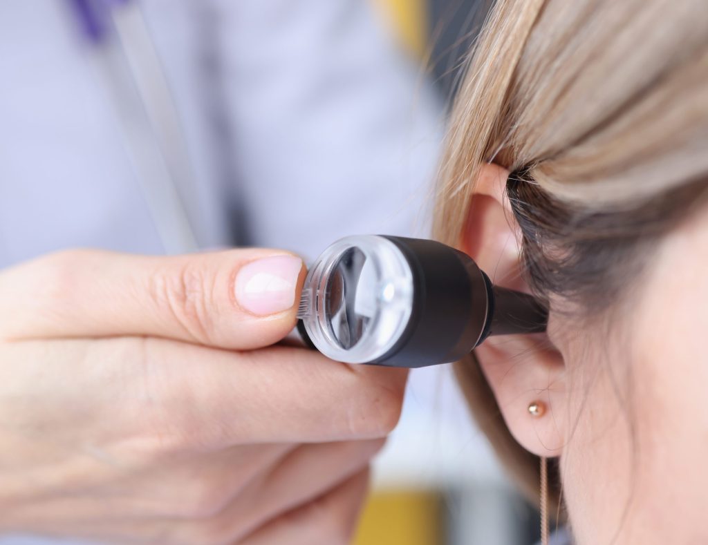 Otorhinolaryngologist looking at patients ear using an otoscope closeup