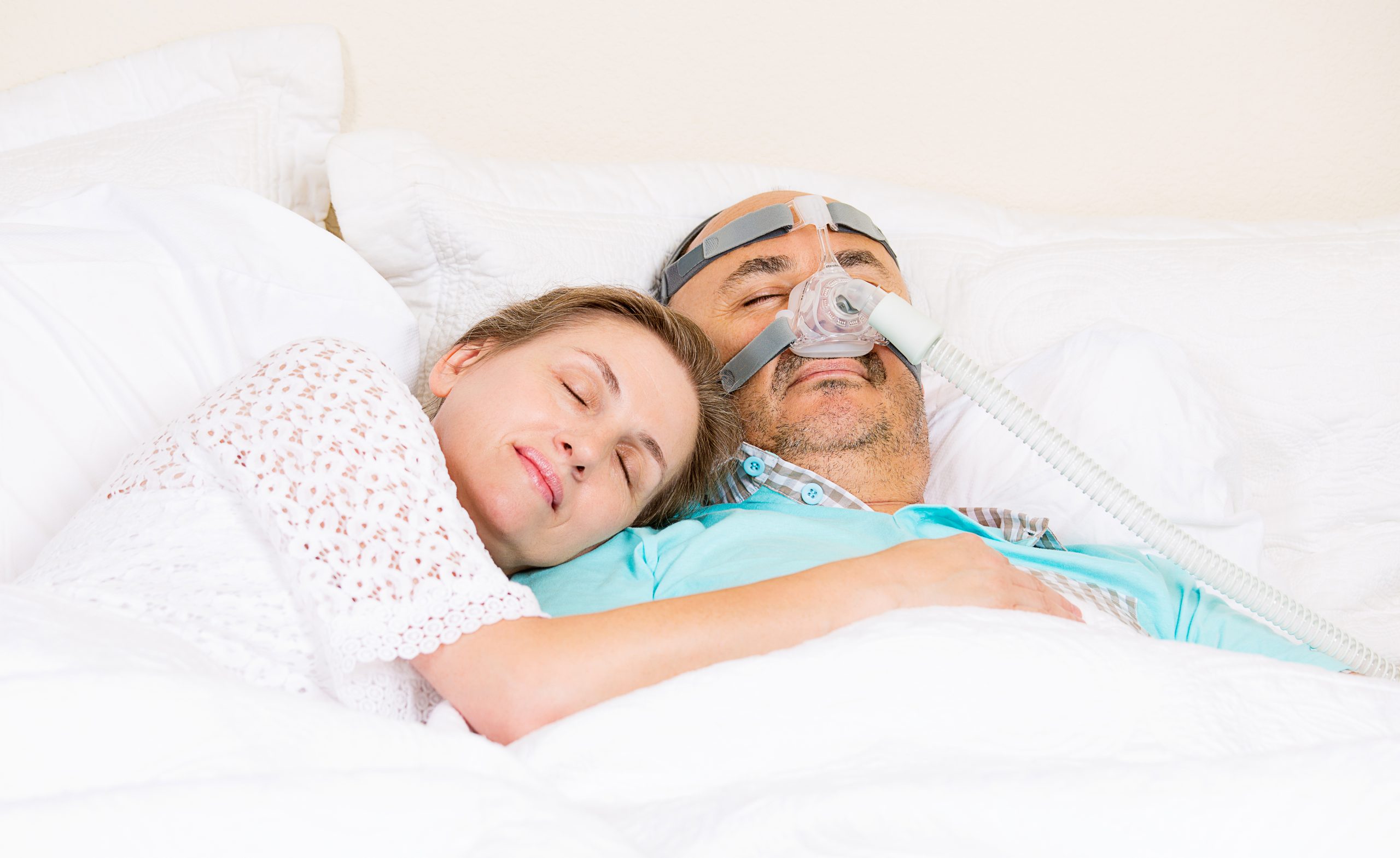 man with sleeping apnea and CPAP machine sleeping peacefully with wife in bedroom
